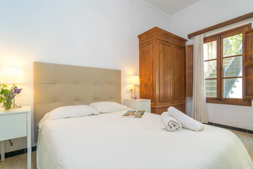 A bright bedroom with a large bed, bedside tables, and a wooden wardrobe.