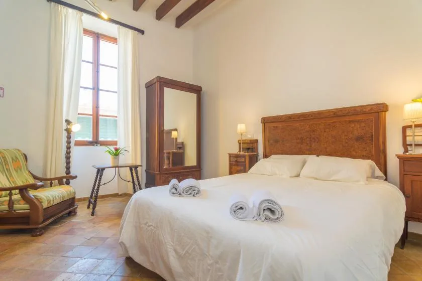 A bedroom with a large bed, wooden headboard, and a sunlit window.