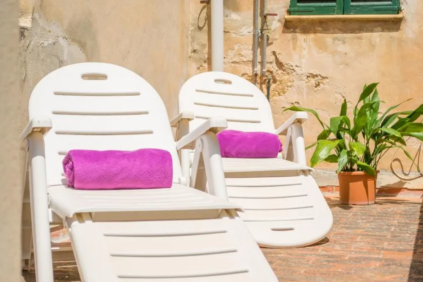 Two white lounge chairs with pink towels sit on a sunlit terrace.