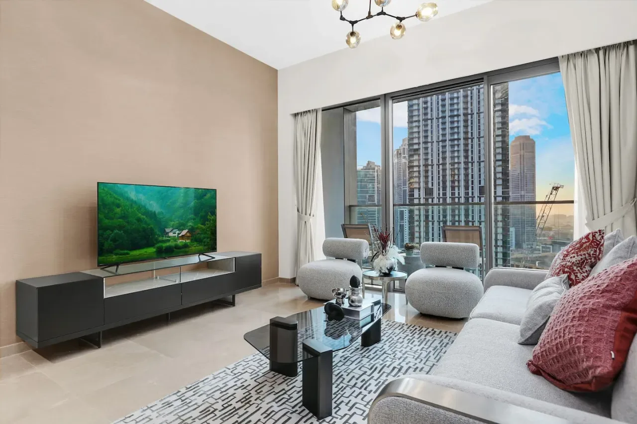 Una sala luminosa con asientos, un televisor y grandes ventanas con vistas a edificios de la ciudad.