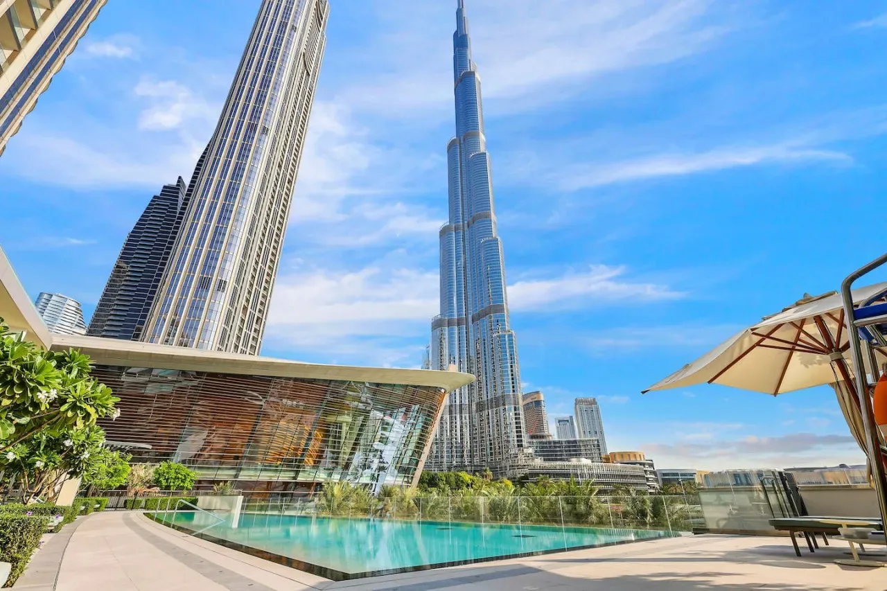 Un paisaje urbano de rascacielos domina una piscina turquesa y una terraza ajardinada.