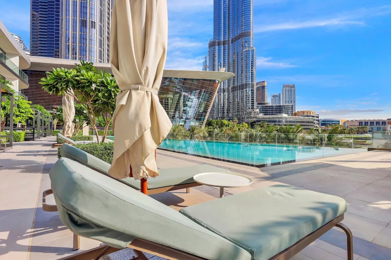Una terraza con piscina y asientos acolchados, con edificios altos de la ciudad al fondo.