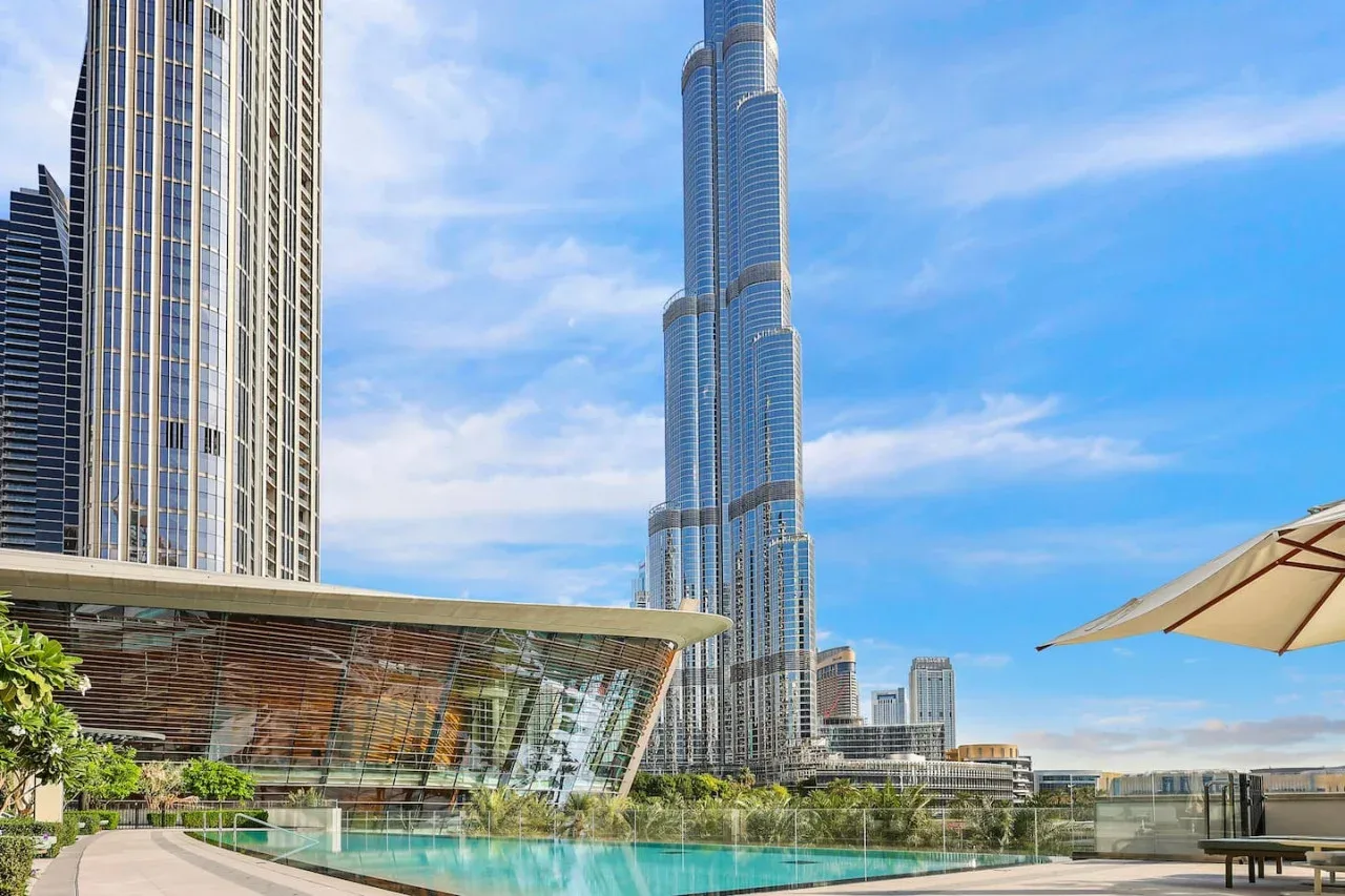 Un horizonte urbano moderno se alza detrás de un edificio acristalado y una piscina al aire libre.