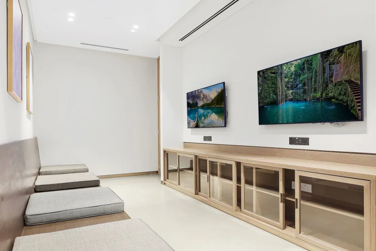 Una sala luminosa con asientos acolchados y pantallas grandes sobre un mueble largo.