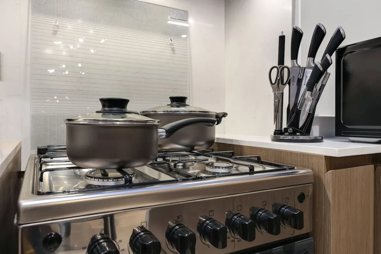 Una estufa de cocina con ollas, junto a una pared de azulejos y utensilios sobre la encimera.