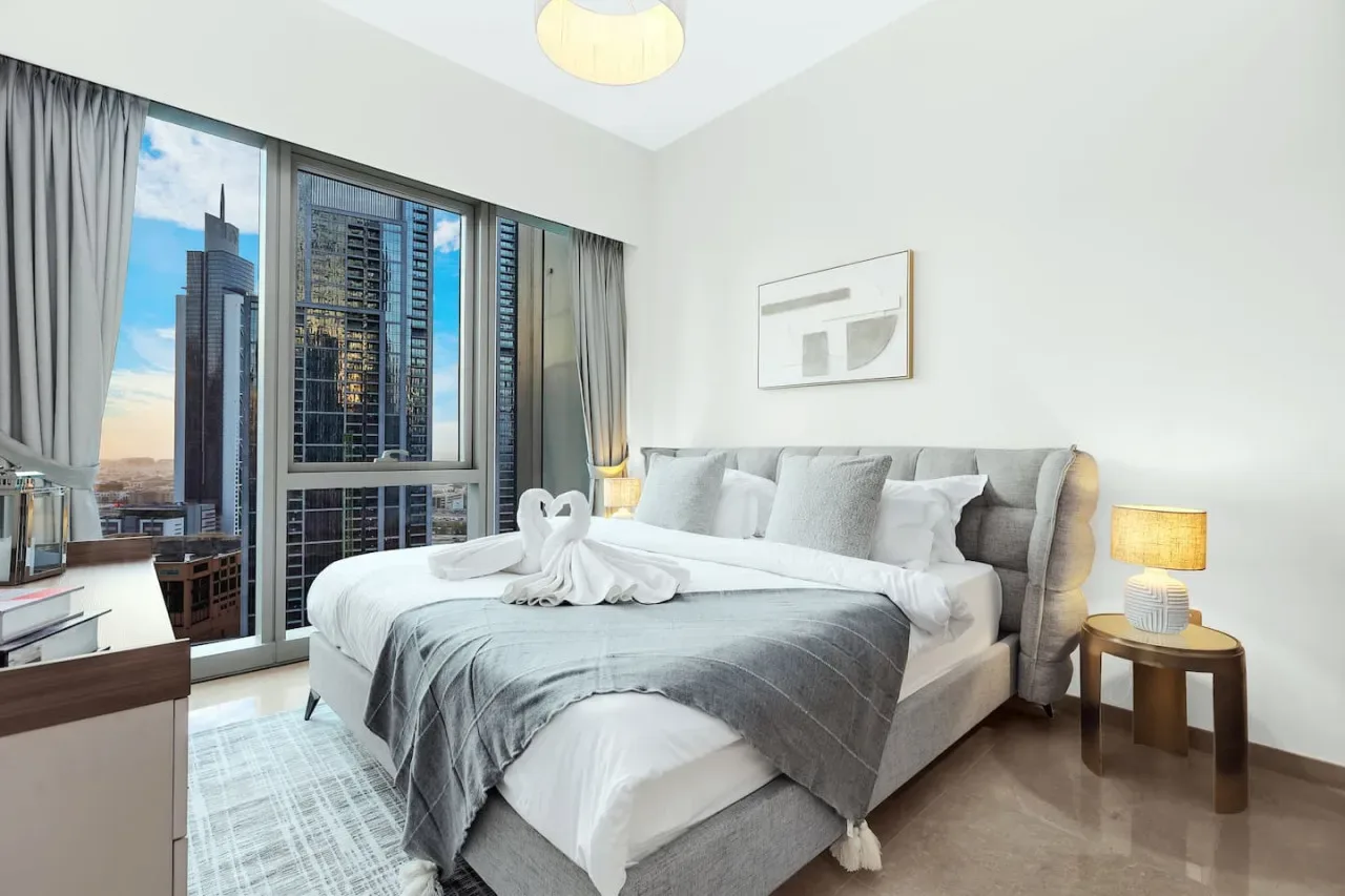 Un dormitorio luminoso con una cama bien hecha junto a grandes ventanas.
