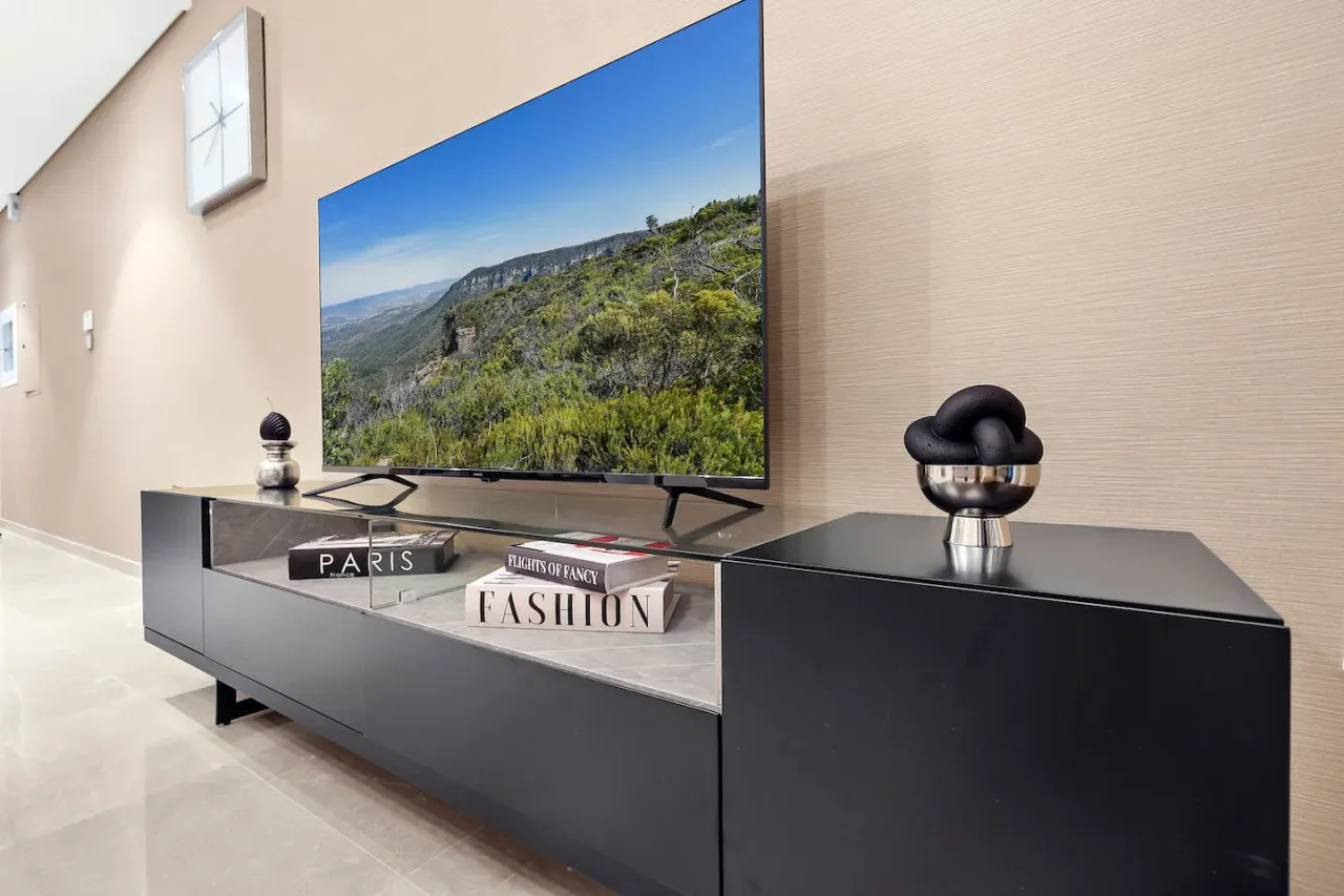 Un televisor con un paisaje montañoso está sobre un mueble multimedia oscuro.