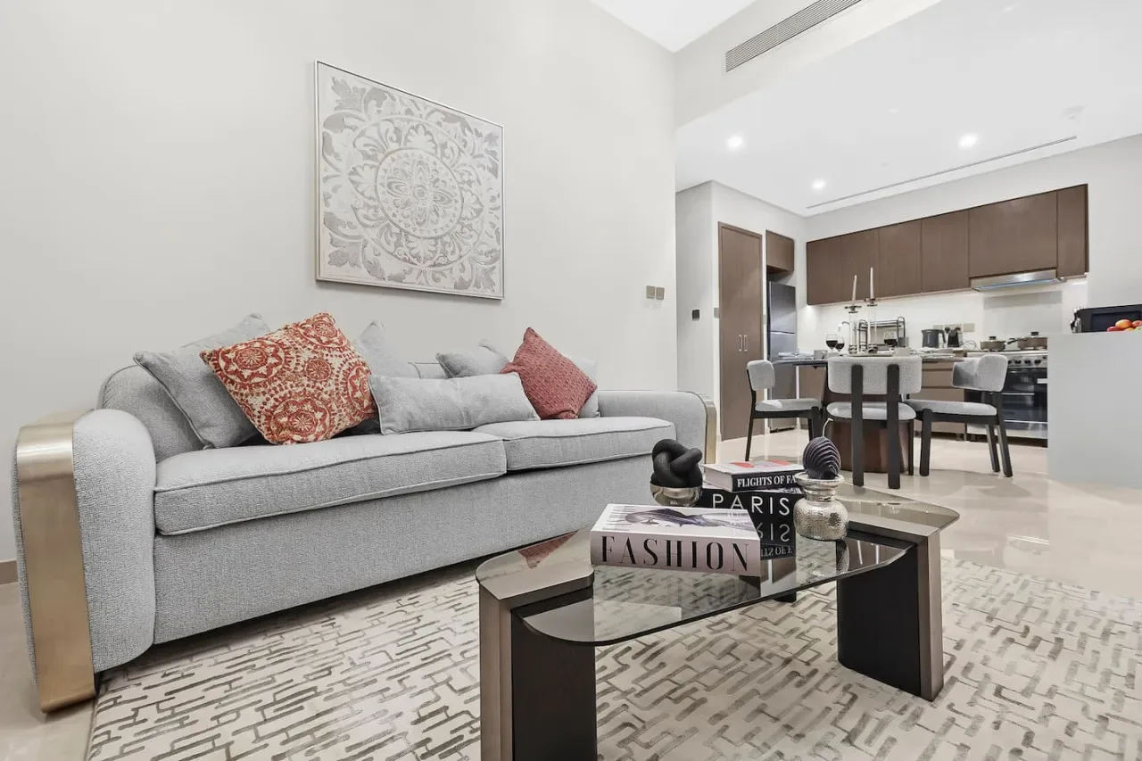 Una sala luminosa con un sofá gris y un comedor al fondo.