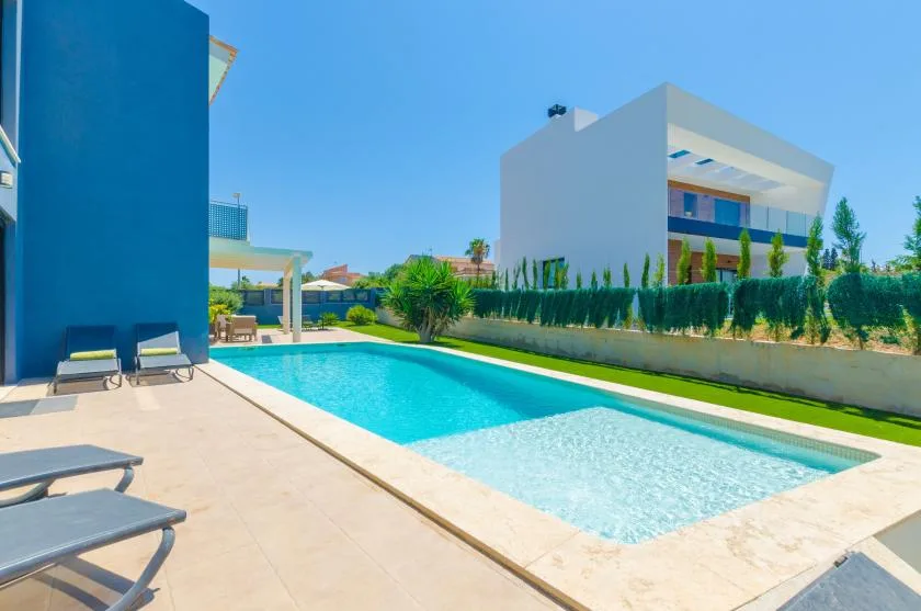 A swimming pool beside modern buildings, with lounge seating in the foreground.