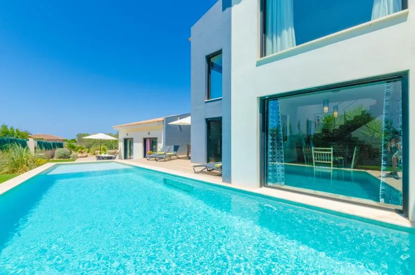 A swimming pool runs alongside a modern white house under a clear blue sky.