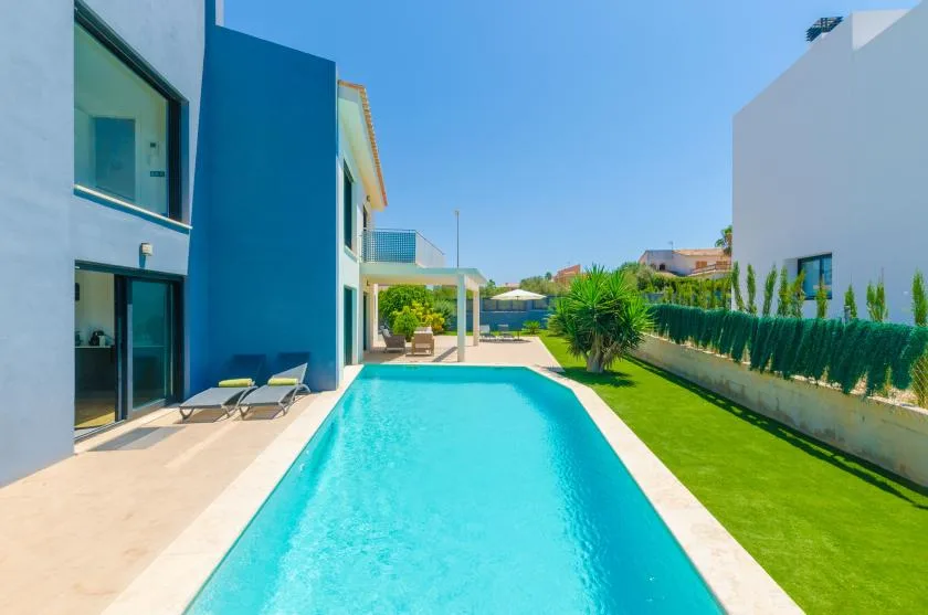A swimming pool beside a modern house and a strip of green lawn.