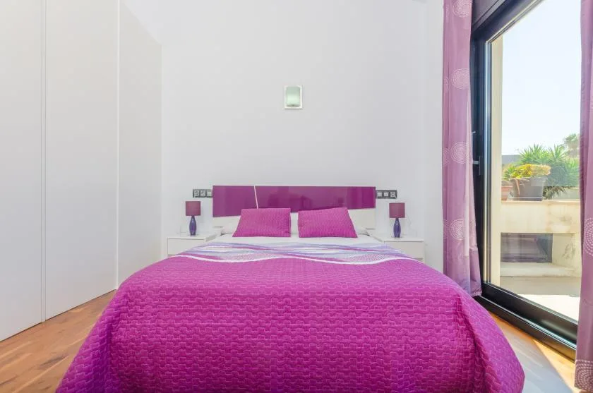 A bedroom with a bed dressed in bright pink bedding beside a glass balcony door.