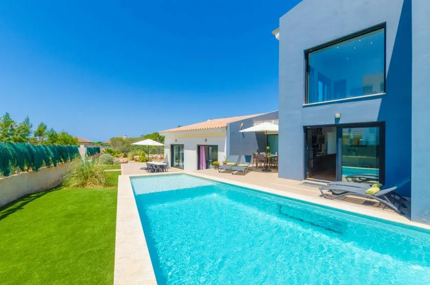 A swimming pool beside a modern house and green lawn.