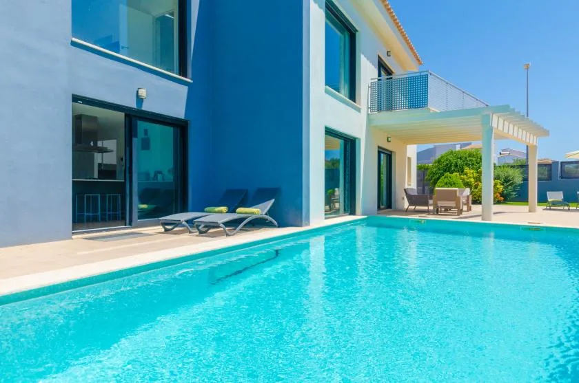 A swimming pool beside a modern building, with loungers along the edge.