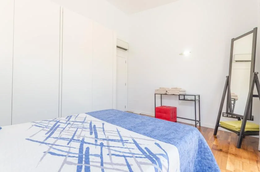 A bedroom with a bed covered in blue and white bedding and a standing mirror.