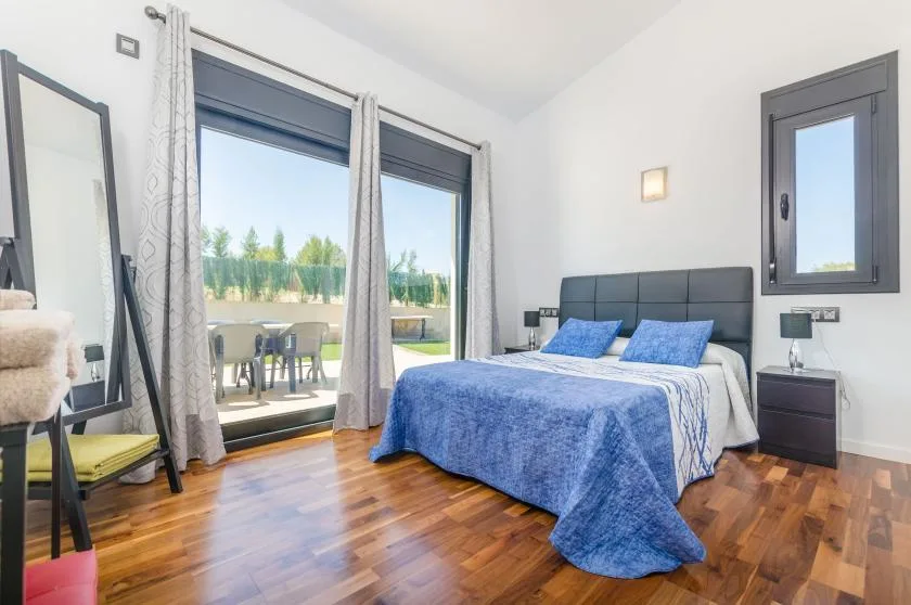 A bedroom with a bed covered in blue bedding beside glass doors.