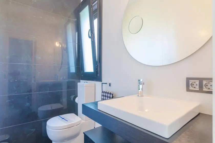 A modern bathroom with a white vessel sink and a window beside the shower.