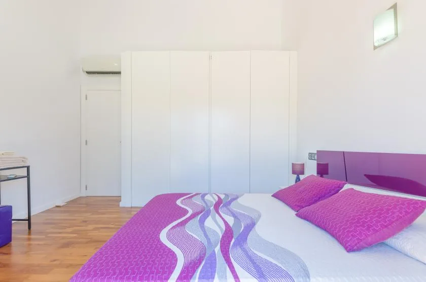 A bedroom with a bed dressed in bright pink and purple bedding.