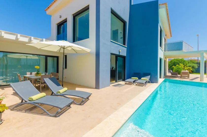 A modern house opens onto a swimming pool and a patio with loungers.