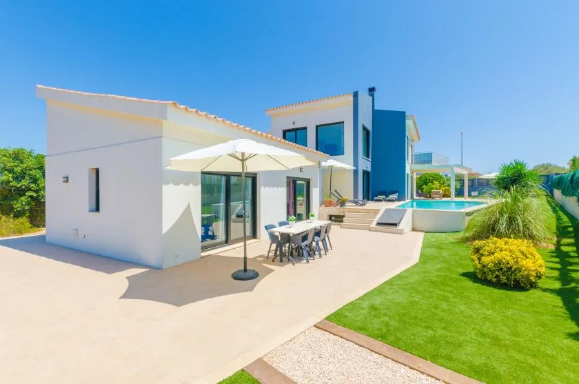 A modern house opens onto a sunny patio with outdoor seating and a pool.