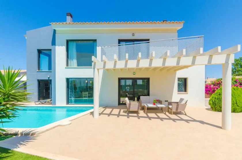 A modern white house opens onto a patio with seating and a swimming pool.