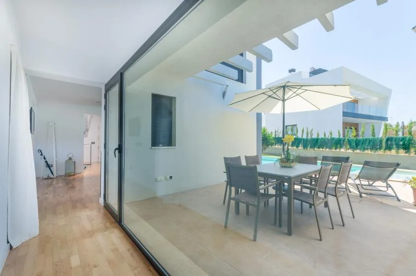 A glass-walled dining area opens onto an outdoor patio with a table and umbrella.
