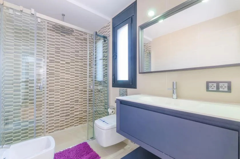 A bathroom with a vanity, mirror, toilet, and glass shower screen.