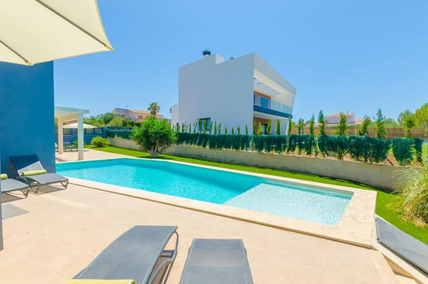 An outdoor swimming pool beside a modern white building, with lounge seating on the patio.