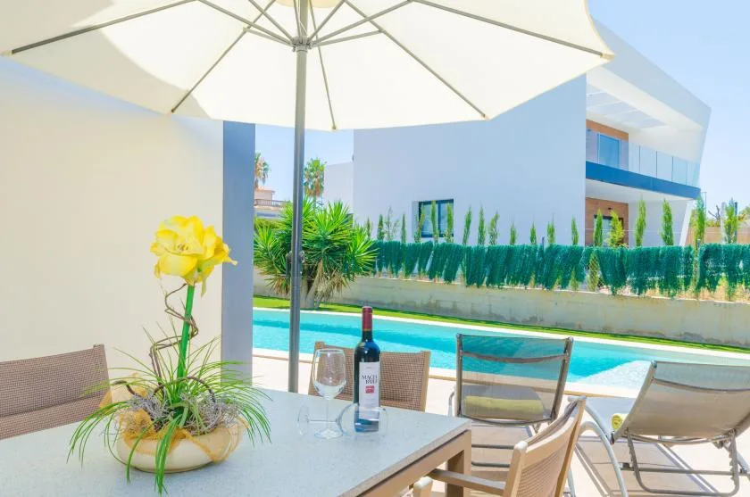 A poolside patio with a dining table, chairs, and a large umbrella.
