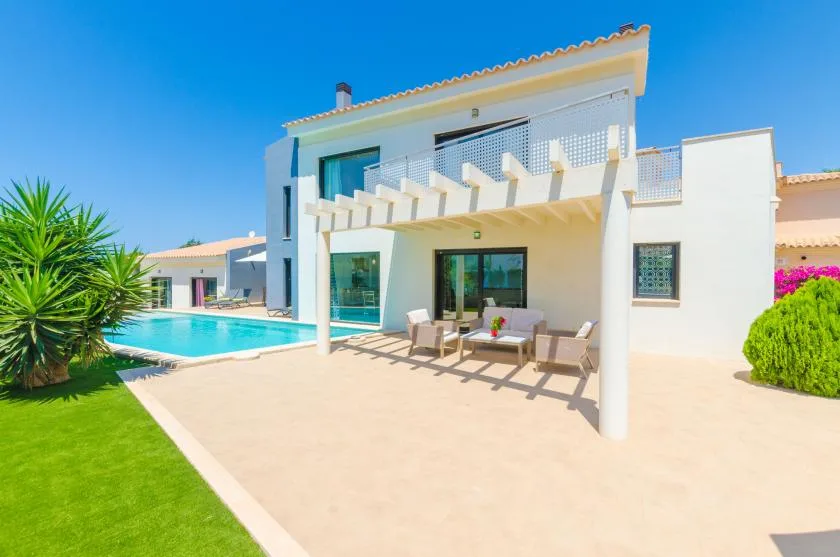 A modern white house opens onto a sunny patio beside a swimming pool.