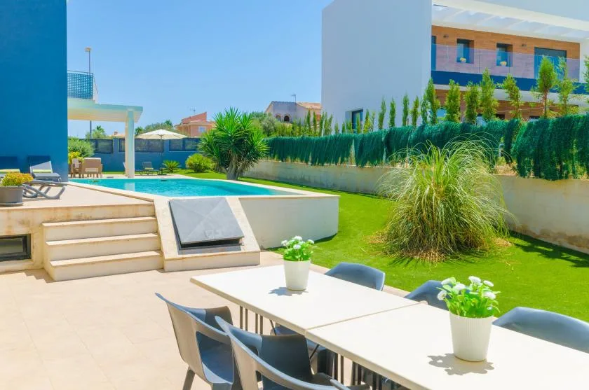 Outdoor dining area beside a swimming pool, with a table and chairs on a sunny patio.
