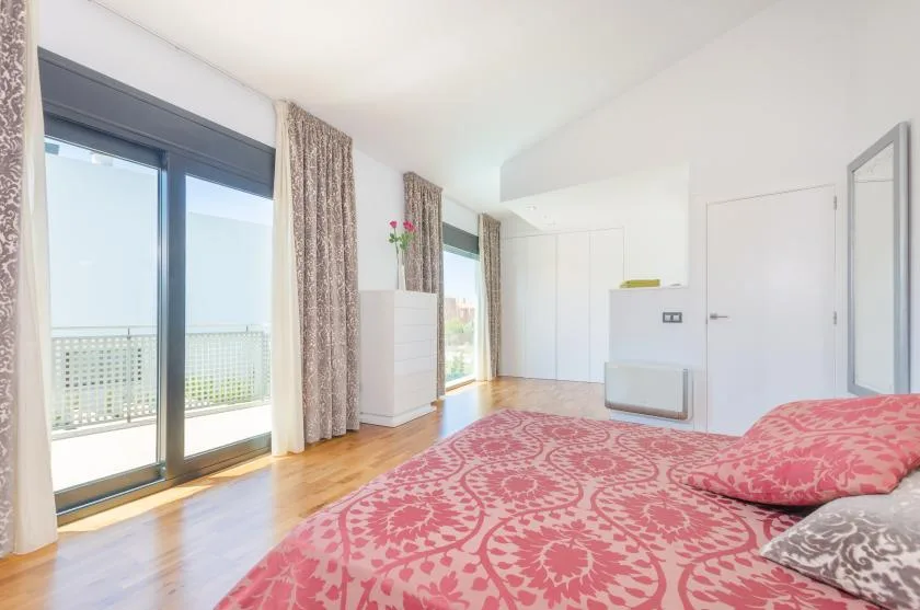 A bright bedroom with patterned bedding and large glass doors opening to a balcony.
