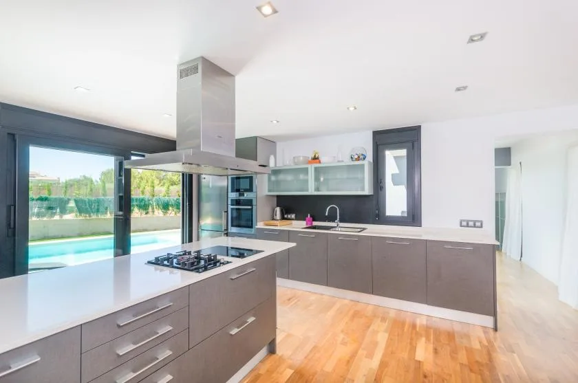 A modern kitchen with an island and large glass doors opening toward a pool.