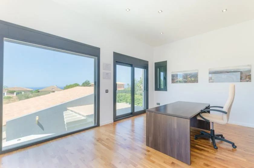 A bright office with a desk and chair beside large windows.
