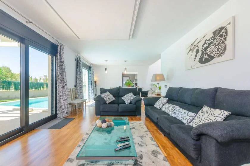 A living room with dark seating, a glass coffee table, and large windows.
