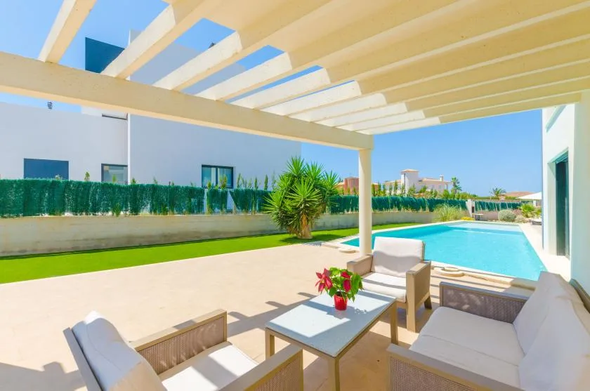 A covered patio seating area overlooks a swimming pool and landscaped lawn.