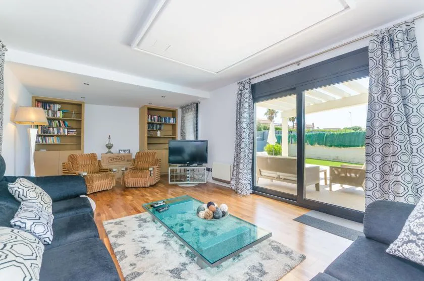 A bright living room with seating, a glass coffee table, and sliding doors to the patio.