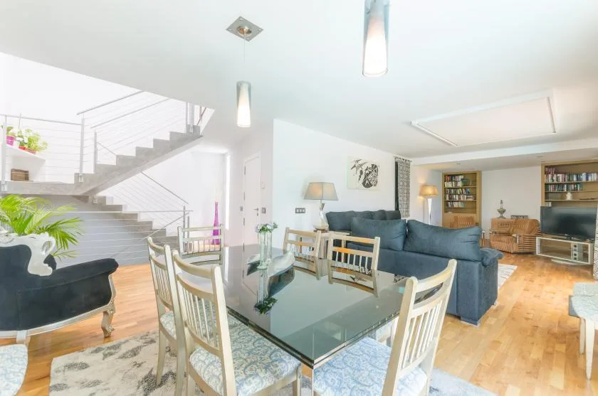A bright living and dining area has a glass dining table and blue seating.
