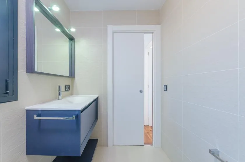 A tiled bathroom with a blue vanity and a large wall mirror.
