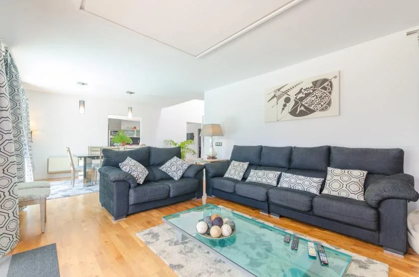 A bright living room with dark seating arranged around a glass coffee table.