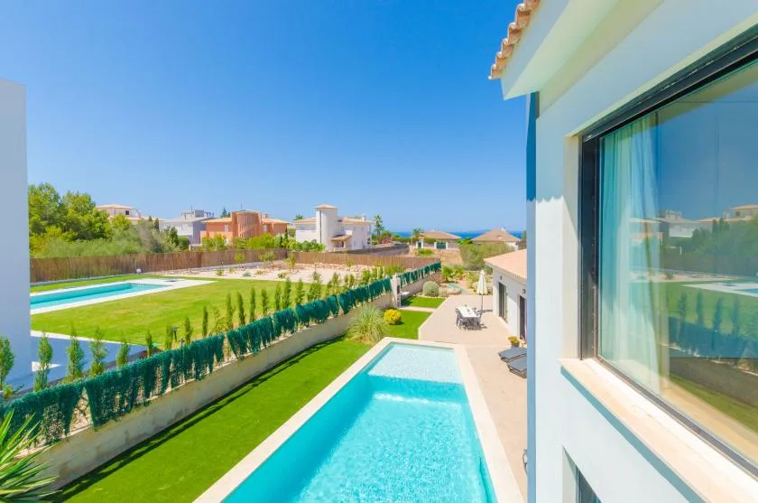 A sunny outdoor pool beside a landscaped yard, with homes and the sea in the distance.
