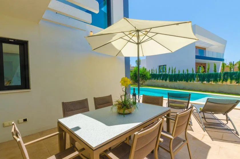 Outdoor dining area beside a swimming pool, shaded by a large umbrella.