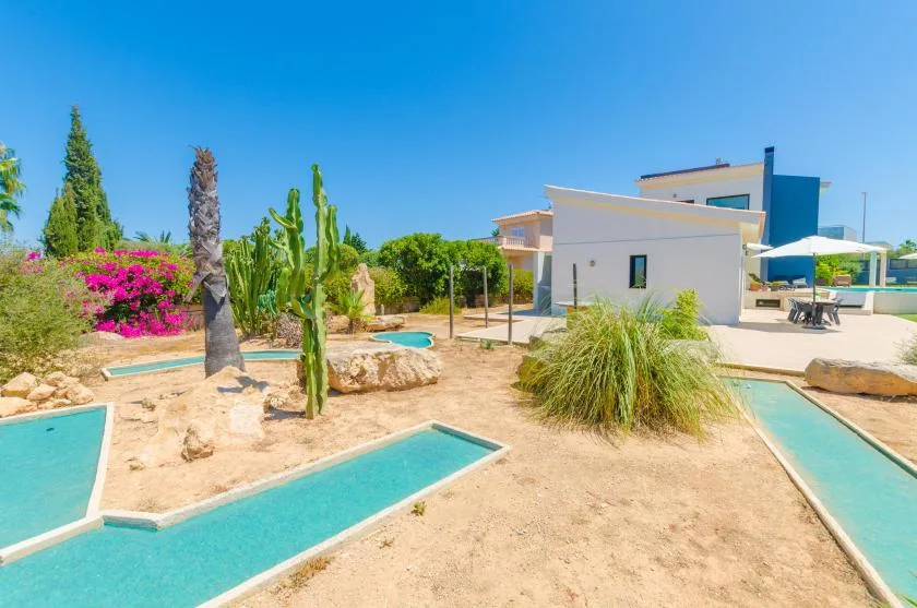A modern house stands beside a turquoise pool in a sunny landscaped yard.