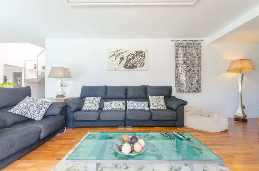 A living room with dark seating, a glass coffee table, and framed wall art.