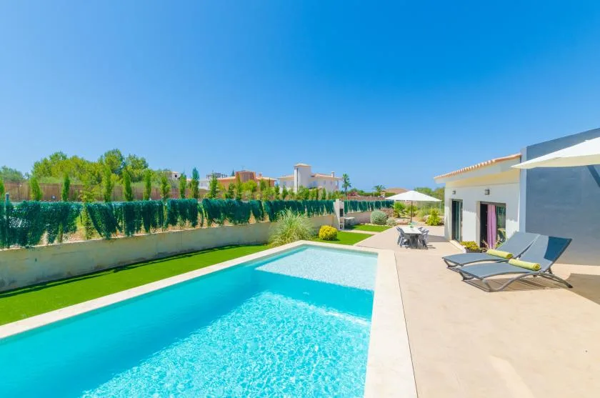 Outdoor swimming pool beside a patio with loungers and a modern building.