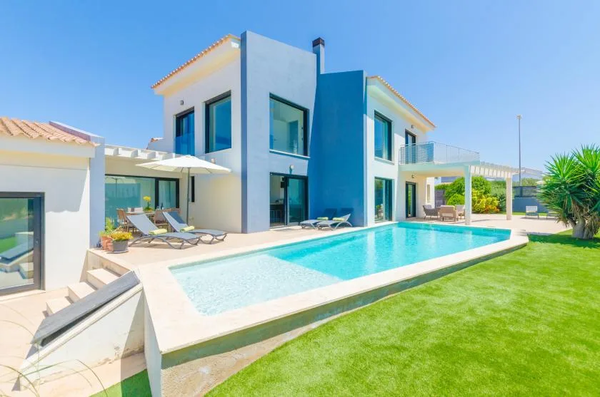A modern house beside a swimming pool and green lawn.