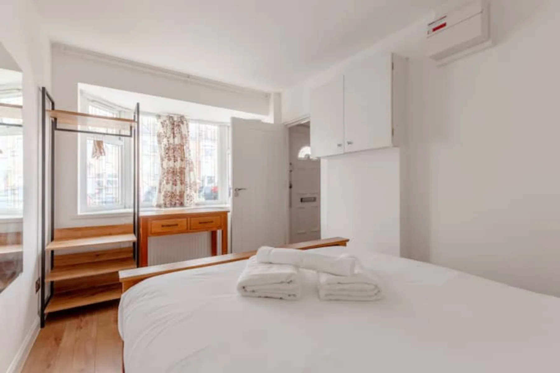 Un dormitorio luminoso con una cama, estantes de madera y una ventana.