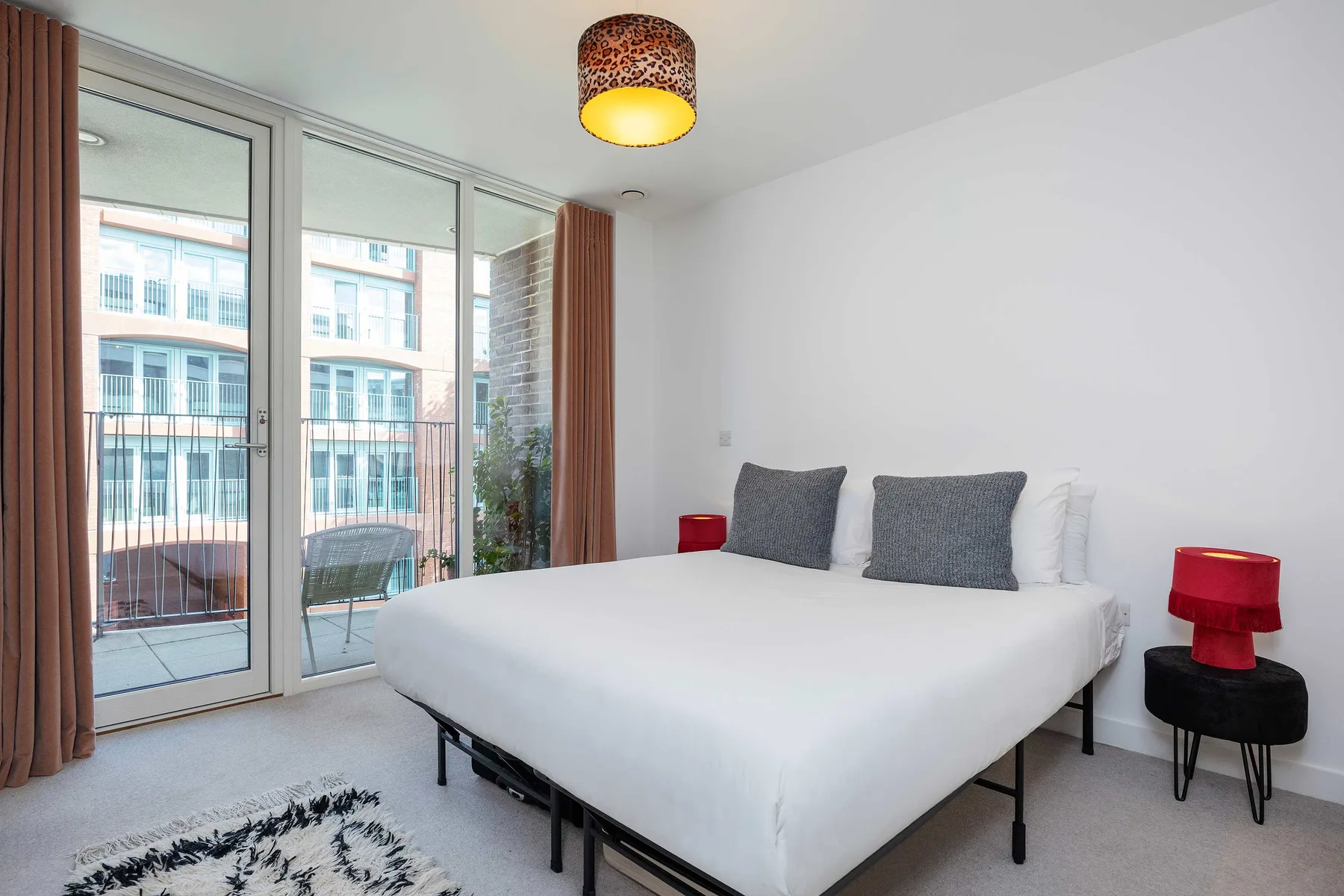 A bedroom with a white bed, gray pillows, and glass doors opening onto a balcony.