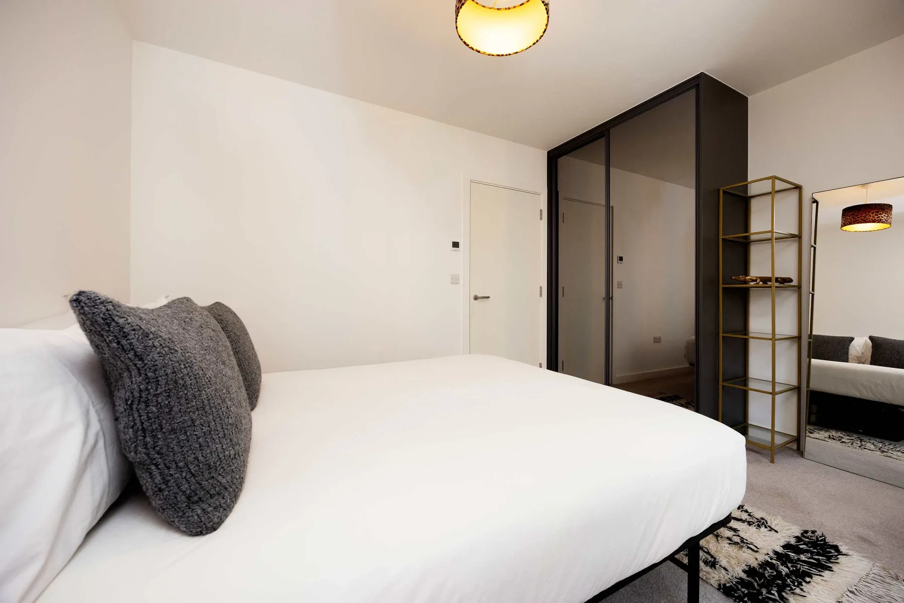 A bedroom with white bedding, a dark wardrobe, and a floor mirror.