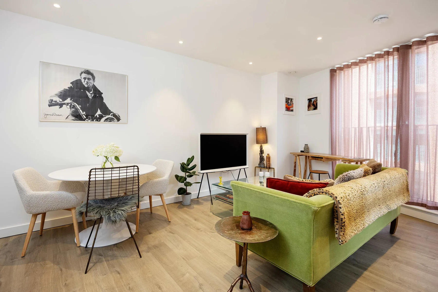 A bright living room with a dining table beside green seating and large curtained windows.